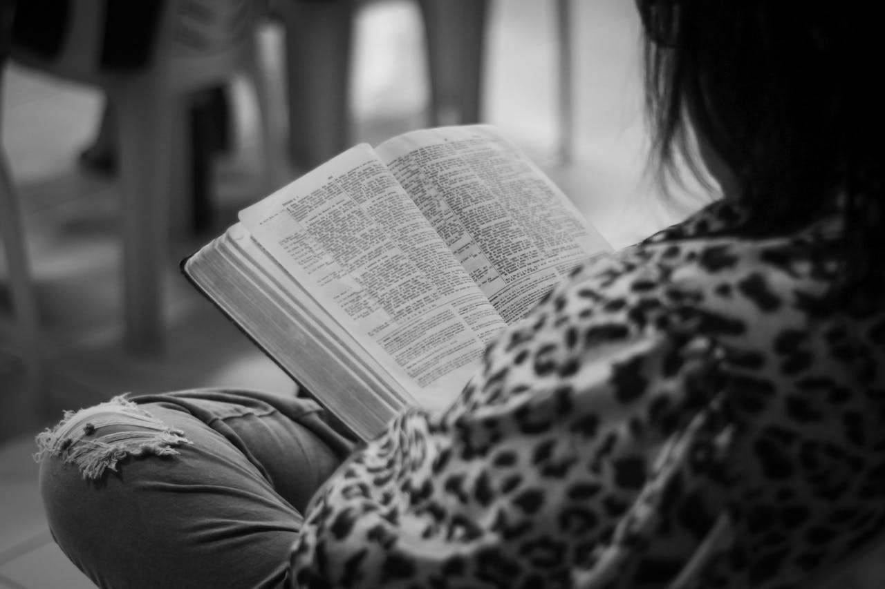 A woman reads a Bible in a monochrome setting, evoking a sense of contemplation.
