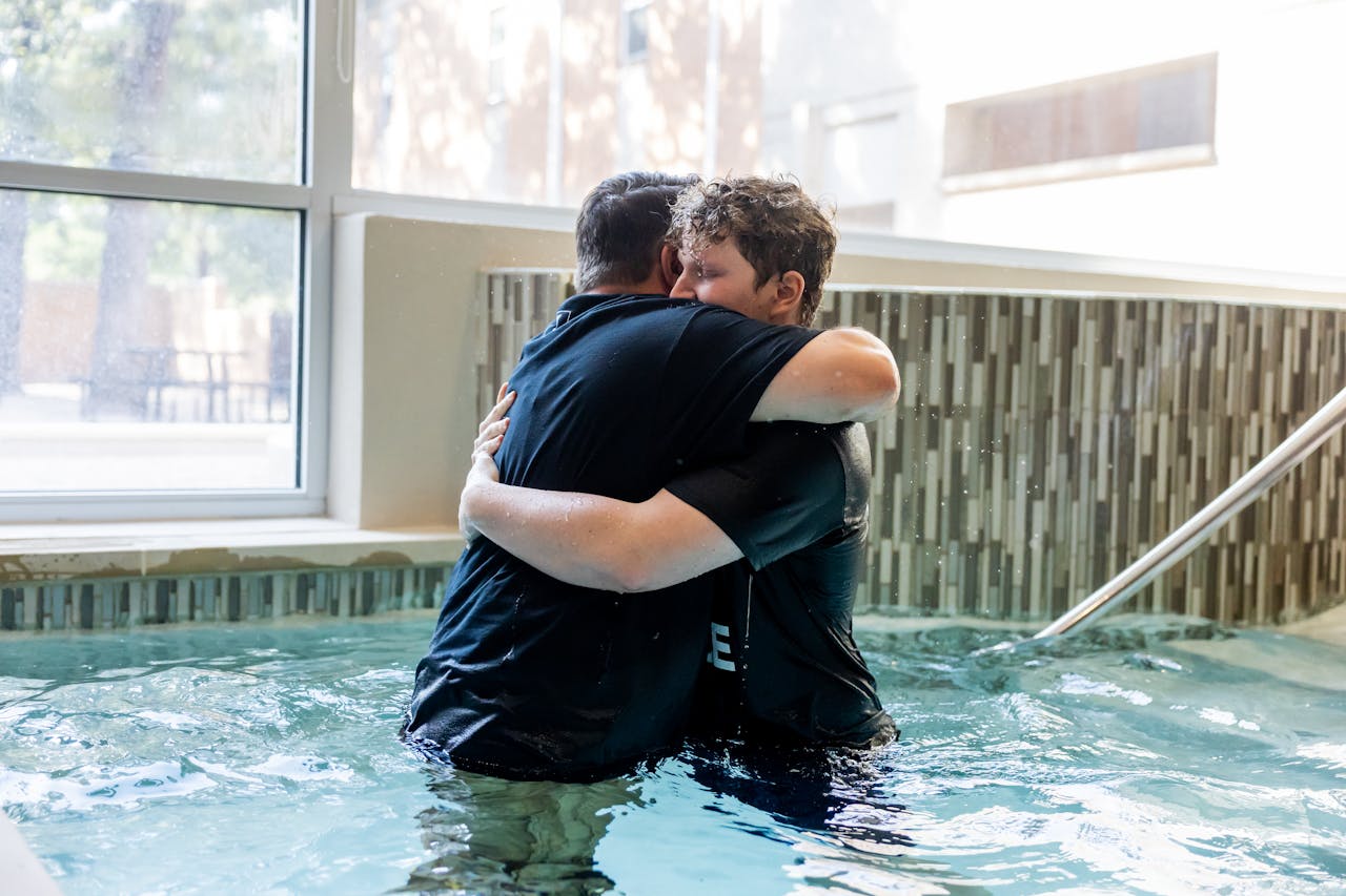 Two men embrace after baptismal ceremony in an indoor pool, symbolizing faith and community.